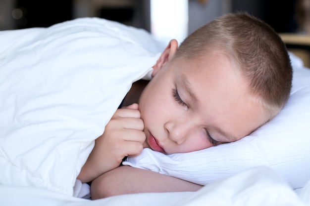 Foto chico lindo en una cama blanca debajo de una manta blanca