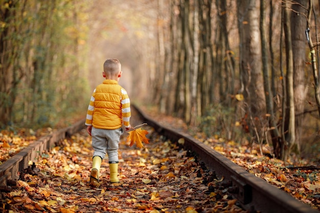 Chico lindo caminando en un ferrocarril sonriendo túnel de amor de tiempo de otoño en lugar romántico de otoño