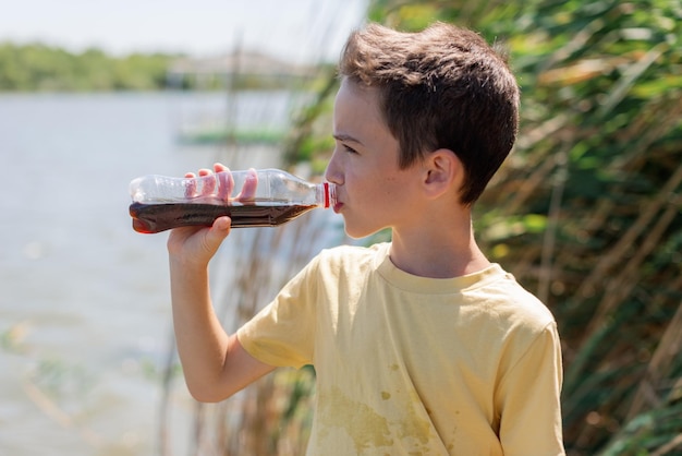 Un chico lindo con una camiseta amarilla sostiene una botella en la mano y bebe limonada Calor de verano