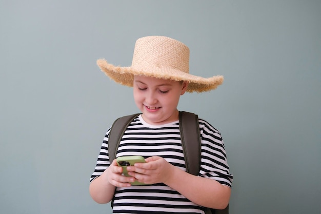 Un chico lindo con camiseta y sombrero con una bolsa sosteniendo y mirando un teléfono móvil con fondo verde