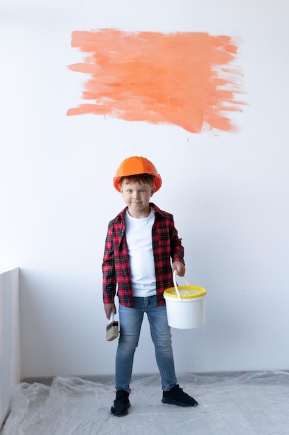 Chico lindo cepillando las paredes Concepto de renovación del hogar El hijo ayuda a sus padres a pintar la pared Pequeño ayudante Baner Copiar espacio