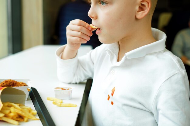 Chico lindo comiendo papas fritas y salsa de tomate en la mesa en un restaurante de comida rápida K