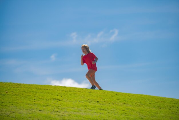 Chico lindo corriendo a través de la hierba y el cielo de verano niño deportivo chico corredor corriendo en el parque de verano activo k