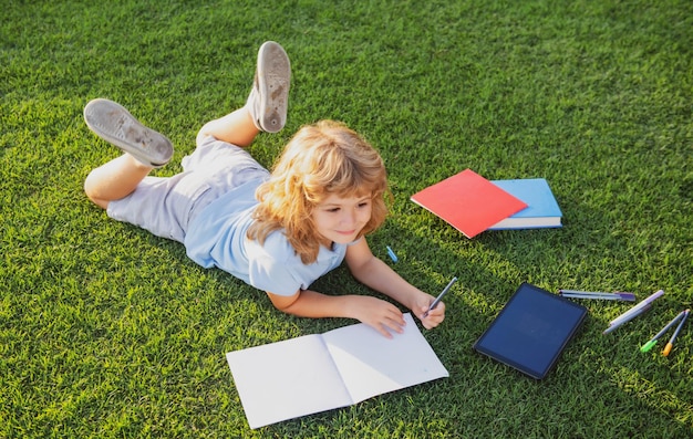 Chico lindo escribiendo en un cuaderno al aire libre Campamento de verano Concepto de aprendizaje y educación para niños
