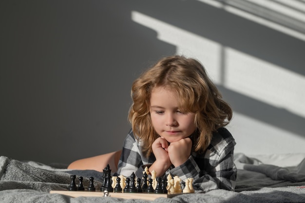Chico lindo está jugando al ajedrez en la cama en casa Niño pensando en ajedrez El concepto de aprender y hacer crecer a los niños Éxito en el ajedrez y ganar Juego de lógica de tablero pasatiempo y estilo de vida de los niños
