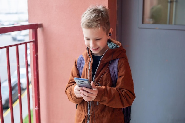 Un chico lindo está de pie con una mochila y un teléfono con auriculares.