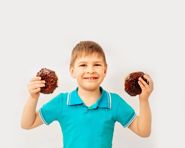 Chico lindo feliz se divierte jugando con donas en una pared de luz. Rosquillas de chocolate