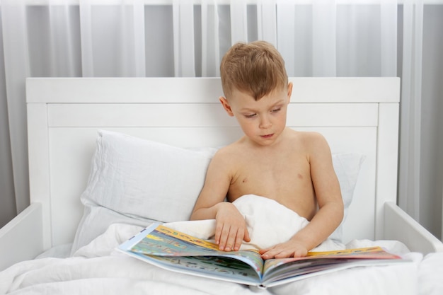 Chico lindo leyendo un libro en una cama blanca