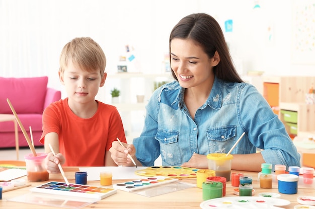 Chico lindo con madre pintando en la mesa en la habitación