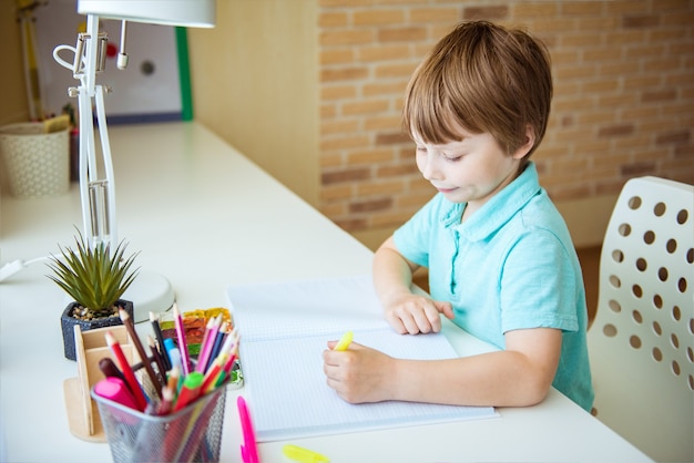 Chico lindo niño haciendo los deberes. Dibujo de niño inteligente en el escritorio. Colegial. Dibujo de estudiante de escuela primaria en el lugar de trabajo. Los niños disfrutan aprendiendo. Educación en casa. De vuelta a la escuela