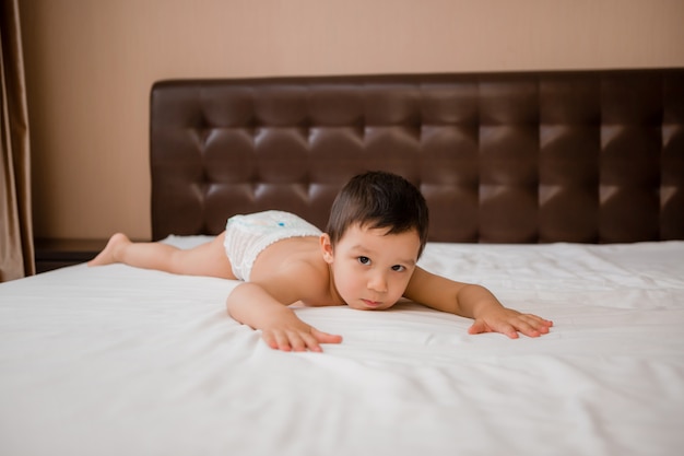 Chico lindo niño en pañales se encuentra en la cama con sábana blanca