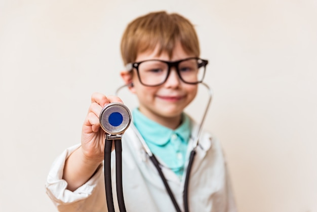 Chico lindo niño pequeño usa gafas de uniforme médico con estetoscopio jugando al doctor