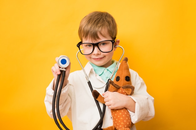 Chico lindo niño pequeño usa gafas de uniforme médico con estetoscopio jugando al doctor