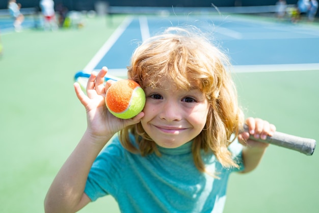 Chico lindo niño con raqueta de tenis en la cancha de la competencia de tenis. Cara de niños graciosos.