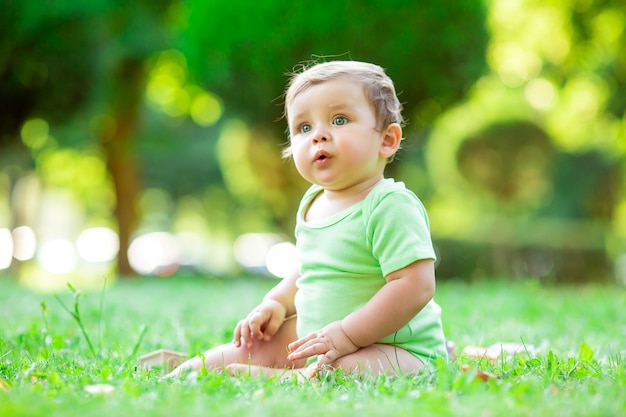 Chico lindo niño en traje verde sentado en el césped