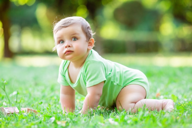 Chico lindo niño en traje verde sentado en el césped