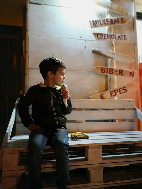 Foto un chico lindo que mira hacia otro lado mientras sostiene un helado por la noche.