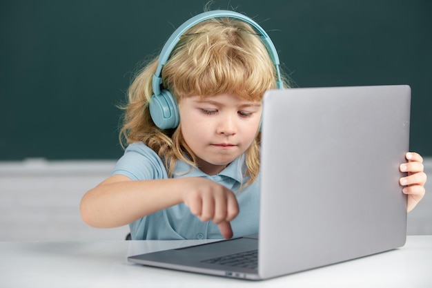 Un chico lindo que usa auriculares estudia con una computadora portátil en el aula escuchando un curso de lección de audio Capacitación en informática