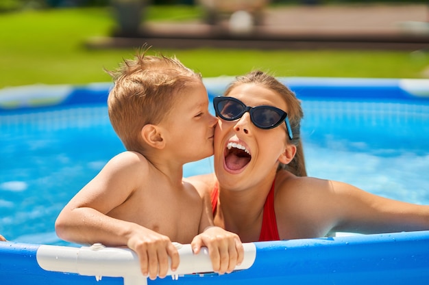 Chico lindo con su madre jugando en una piscina de agua durante el verano