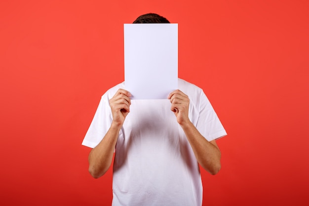 Foto chico lindo con tarjeta blanca en blanco delante de su cabeza, fondo rojo studio