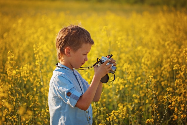 Chico lindo toma fotos de flores en un campo amarillo en verano