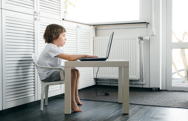 Foto un chico lindo usando una computadora portátil en la mesa.