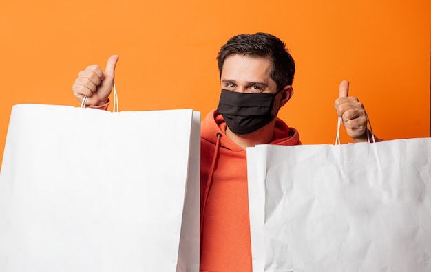 Chico en mascarilla y con bolsas de compras en naranja