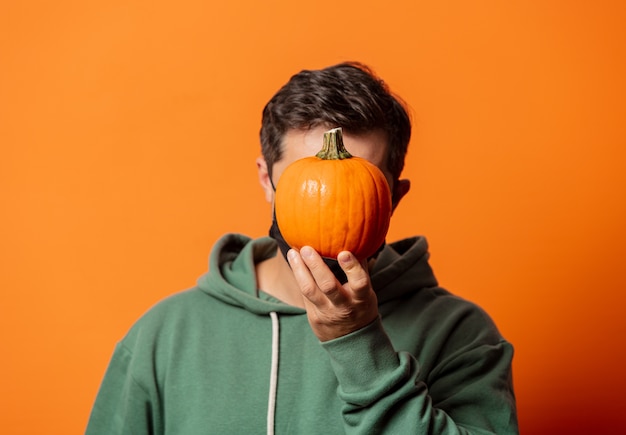 Chico en mascarilla y sudadera con capucha verde con calabaza en naranja