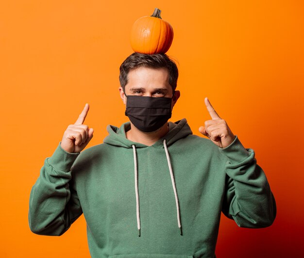 Chico en mascarilla y sudadera con capucha verde con calabaza en naranja