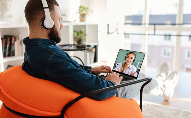 Chico milenario que usa auriculares inalámbricos y una computadora portátil que llama a un socio comercial