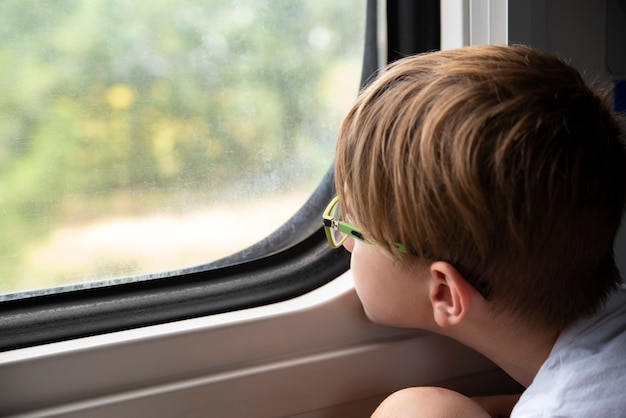Chico mira pensativo por la ventana del tren. Viajar en tren con niños. Viaja en tren.