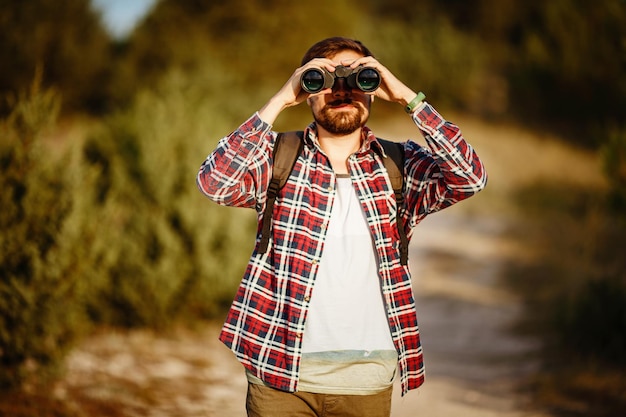 Foto chico mirando binoculares en colina hombre en camiseta con mochila