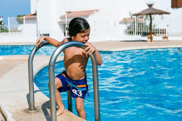 Chico mojado recién salido de la piscina, mira al agua y sonríe divertido