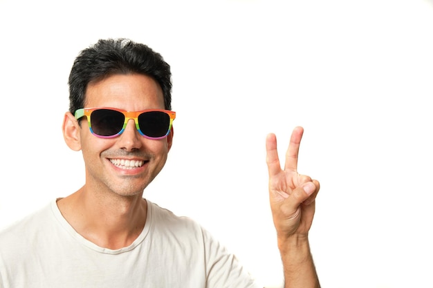 Chico moreno sonriendo con gafas lgbtq de arco iris sobre fondo blanco