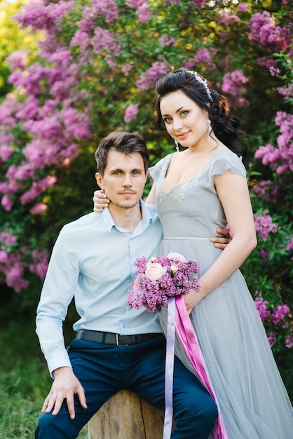 Un chico y una mujer caminan en el jardín de primavera de lilas antes de la ceremonia de la boda