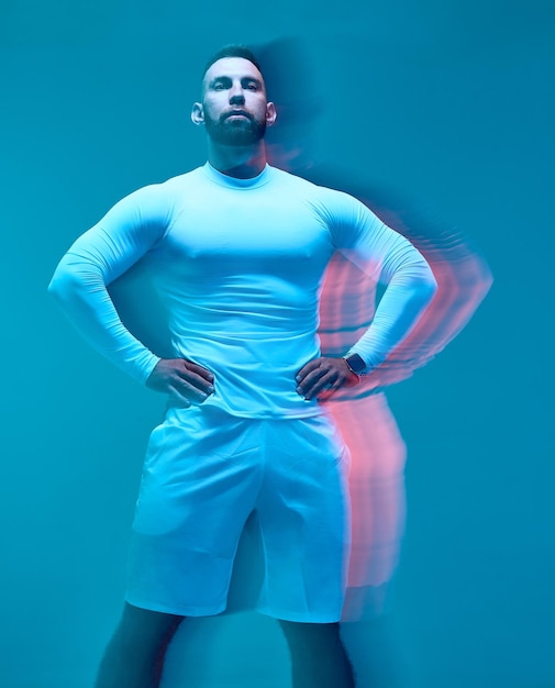 Chico musculoso atlético con ropa deportiva blanca moderna posando sobre fondo azul de estudio largo
