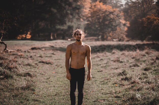 Foto chico musculoso guapo sin camisa sonriendo en medio de un bosque