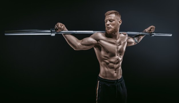 Chico musculoso joven posando con una barra sobre los hombros sobre un fondo negro. Concepto de fitness y nutrición. Técnica mixta