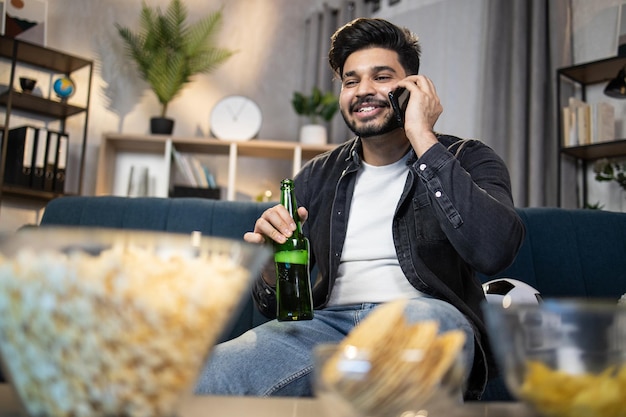 Chico musulmán con smartphone y cerveza viendo fútbol