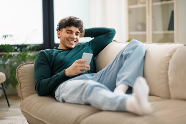 Chico navegando por Internet en el teléfono inteligente acostado en el sofá en casa