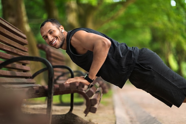 Chico negro deportivo haciendo ejercicio al aire libre empujando desde el banco