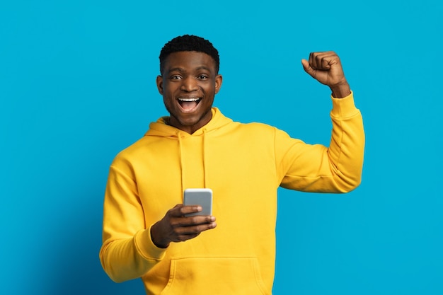 Un chico negro emocional y gracioso usando un teléfono inteligente gestando con emoción