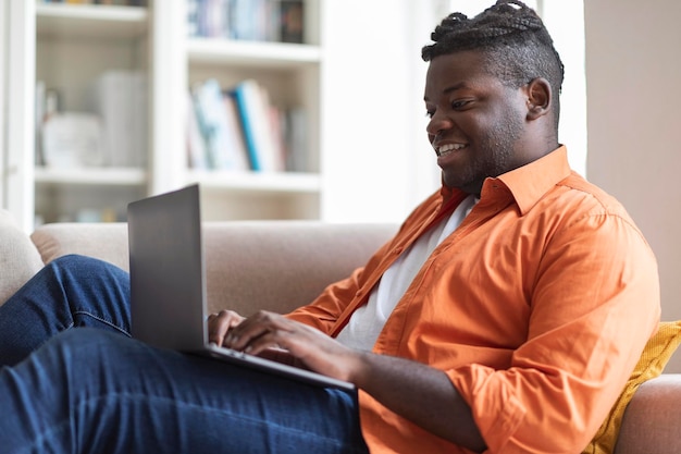 Chico negro gordito feliz usando la computadora portátil en casa