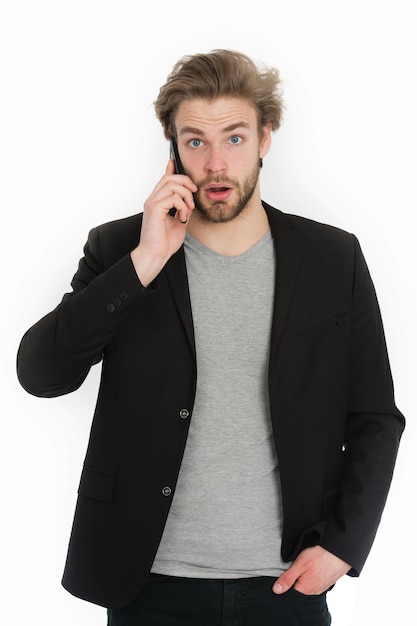 Chico o joven barbudo con chaqueta formal usando un dispositivo de teléfono móvil sorprendido chico aislado sobre fondo blanco.