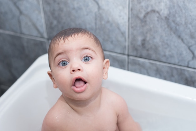 Chico de ojos azules bañándose en la bañera