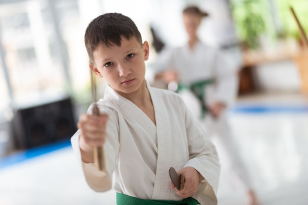 Chico de ojos oscuros. Niño de ojos oscuros en kimono blanco estudiando artes marciales con modelo de cuchillo