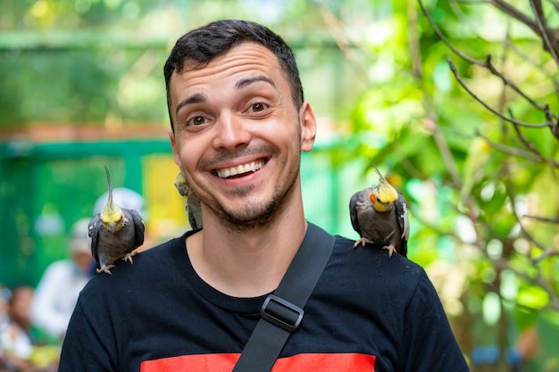 El chico del parque de aves se comunica con los loros. Los loros domesticados piden comida a los turistas.