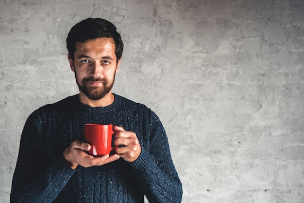 Chico de pelo oscuro tiene una taza roja en la mano sobre un fondo gris