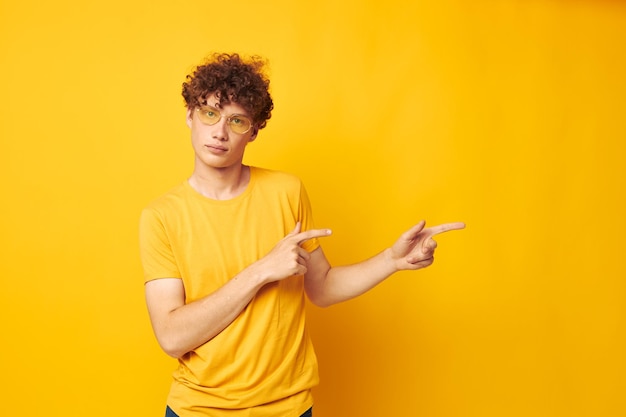 Chico con pelo rizado rojo camiseta amarilla gafas moda gestos con las manos fondo amarillo inalterado