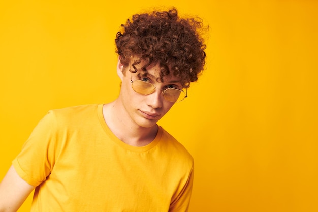 Chico con pelo rizado rojo gafas de estilo juvenil studio ropa casual fondo amarillo inalterado